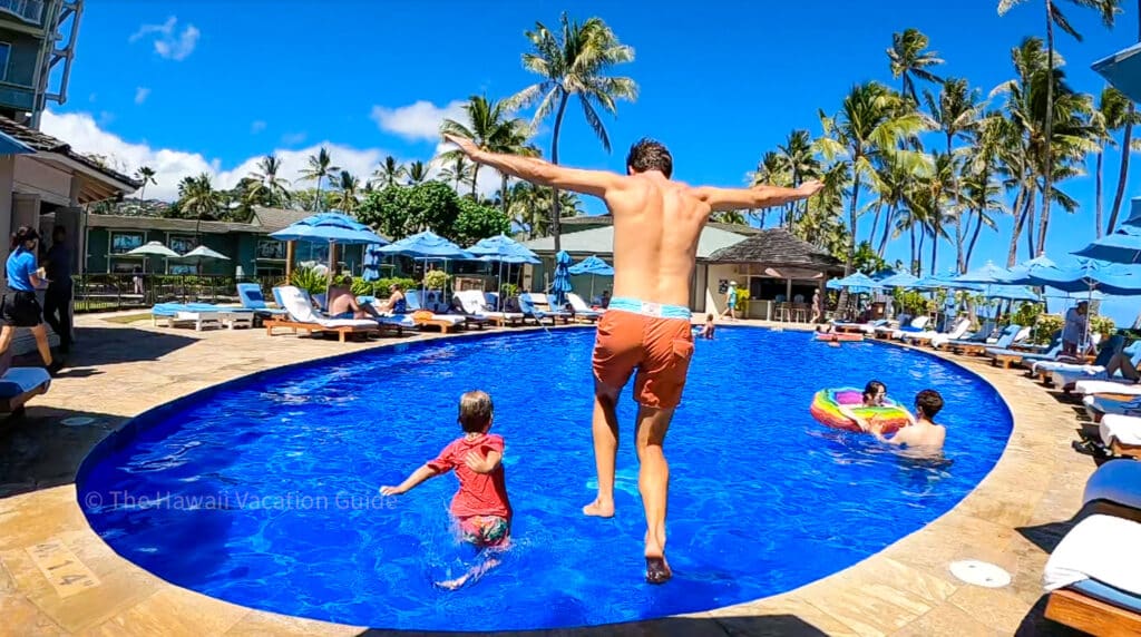 A father and son jumping into an oval shaped pool at the Kahala Hotel, one of the best family resorts in Hawaii