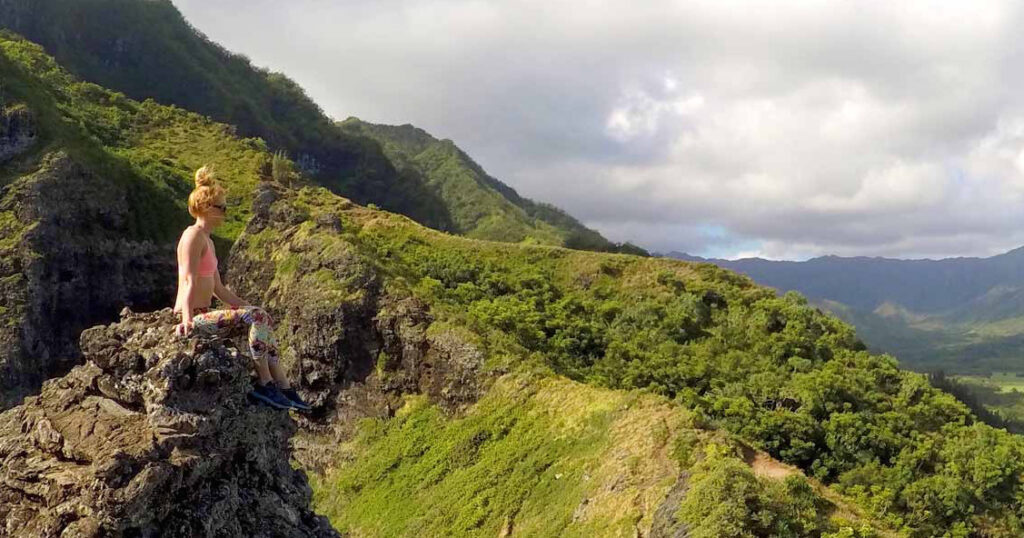 Woman sitting atop rocks overlooking a mountainous island view. Oahu adventure tour